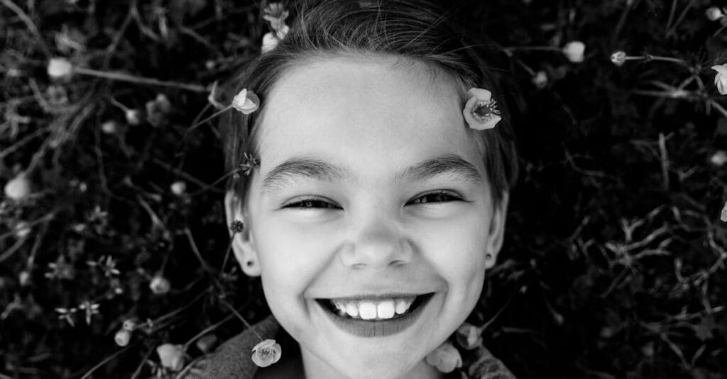 Charming black and white portrait of a smiling child surrounded by nature.