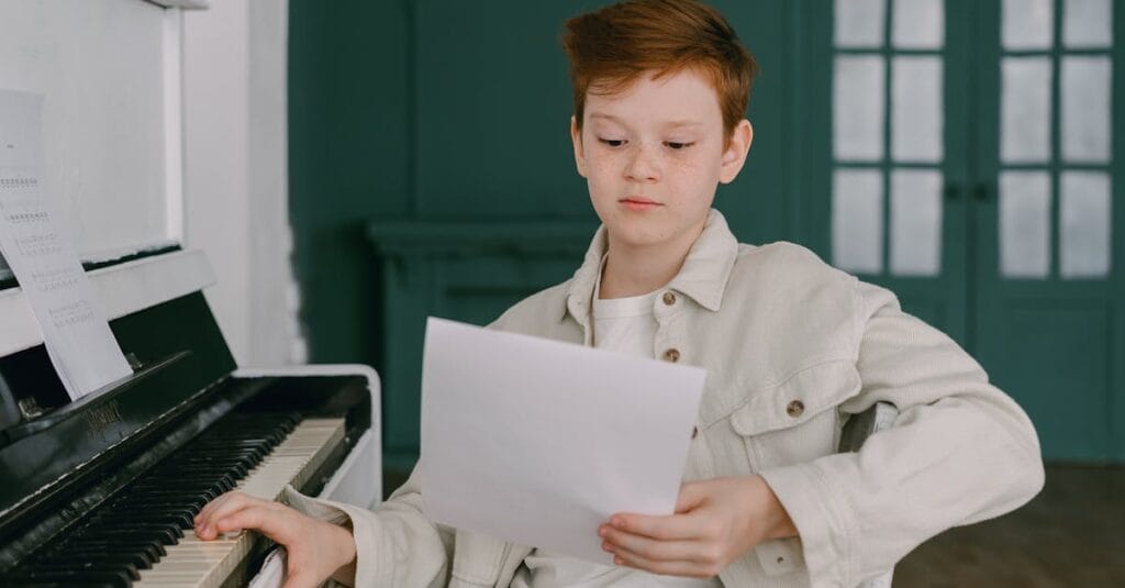 A young boy sits at a piano, reading sheet music, focused on learning indoors.