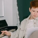 A young boy studying a piano sheet indoors, enhancing musical skills.