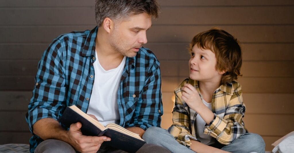 A father and son share a bonding moment reading together indoors, fostering family connection.