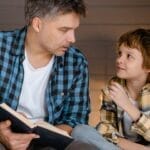 A father and son share a bonding moment reading together indoors, fostering family connection.