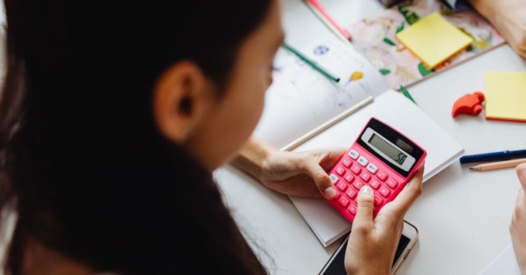 Young girl solving math problems with a pink calculator indoors.