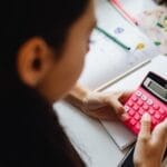 Young girl solving math problems with a pink calculator indoors.