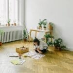 A young girl at home, deeply engrossed in art and craft activity on a wooden floor.