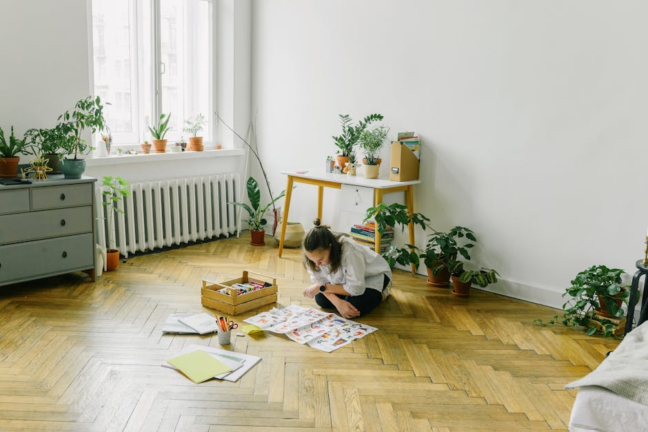 A young girl at home, deeply engrossed in art and craft activity on a wooden floor.
