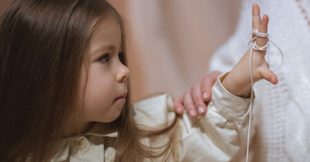 A mother and daughter bonding through a playful yarn activity indoors, highlighting love and connection.