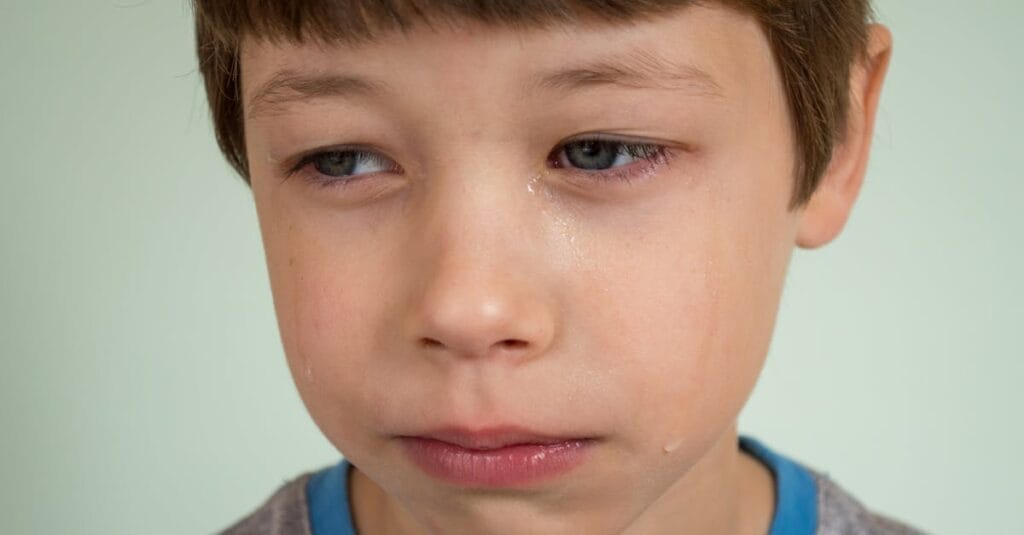 Emotionally expressive portrait of a young boy looking sad with tears on his face.