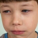 Emotionally expressive portrait of a young boy looking sad with tears on his face.