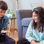 Smiling siblings playing with a spinning top on the floor in a cozy living room.