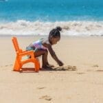 Cute child playing with sand on a sunny beach with ocean waves in the background.