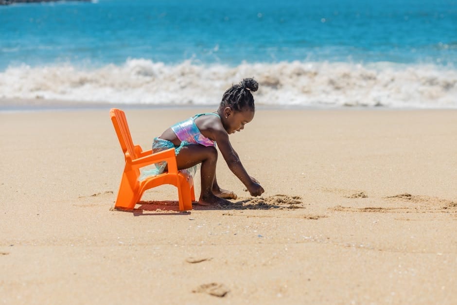 Cute child playing with sand on a sunny beach with ocean waves in the background.