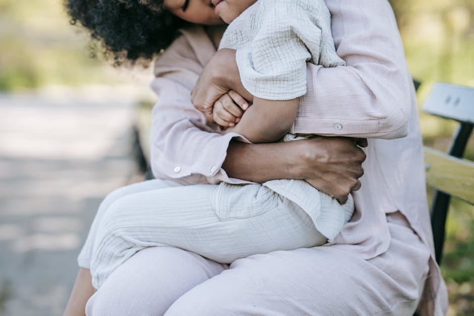 A mother lovingly embraces her child on a wooden bench in a serene outdoor setting.