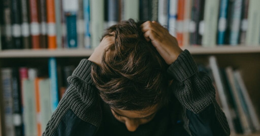 A child appears stressed and frustrated while seated in a library, holding their head.