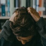 A child appears stressed and frustrated while seated in a library, holding their head.