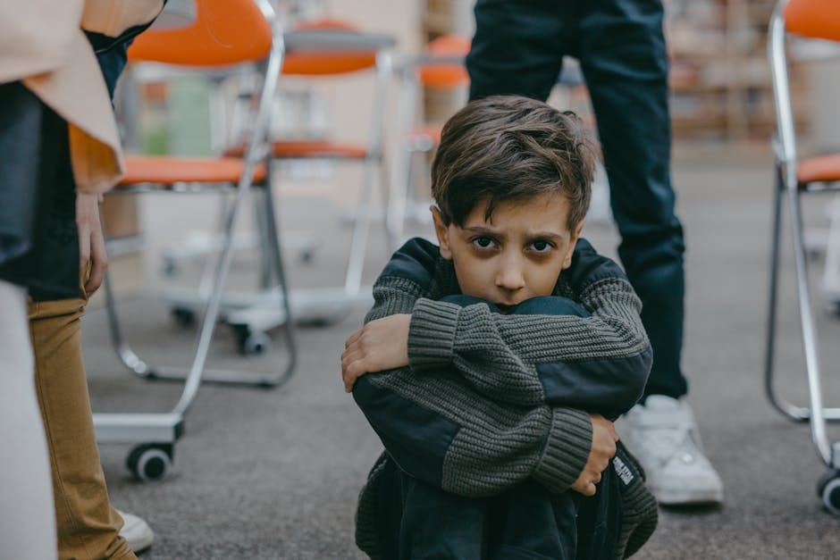 A young boy sits on the floor of a classroom, expressing fear and vulnerability.