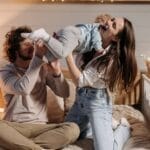 Joyful parents playing with their child on a bed in a warmly lit bedroom.