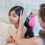 A mother lovingly combs her daughter's hair, fostering a close bond in a cozy bedroom setting.