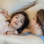 A loving mother embraces her daughter with Down syndrome in a cozy bedroom setting.