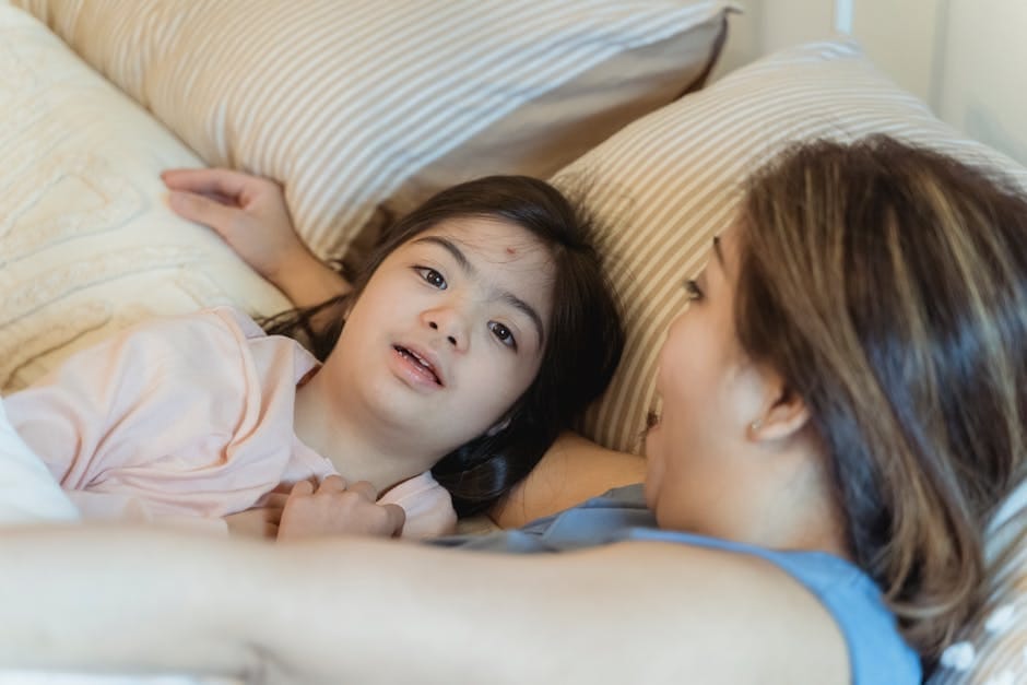 A loving mother embraces her daughter with Down syndrome in a cozy bedroom setting.
