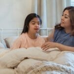 A mother lovingly embraces her daughter in a cozy bedroom setting, expressing warmth and care.