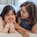 Tender moment between a mother and her daughter with Down syndrome, smiling in bed.