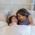 A loving moment between mother and daughter in a cozy bedroom setting.