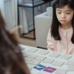 Young girl with Down syndrome focuses on a memory game at a home table.