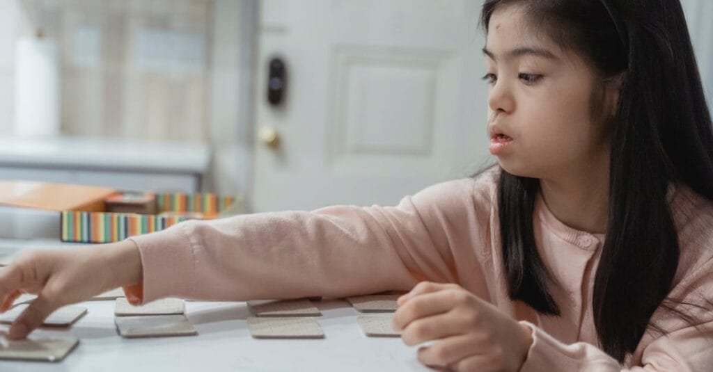 Young Asian girl with Down Syndrome engaged in a game indoors, wearing a pink sweater.