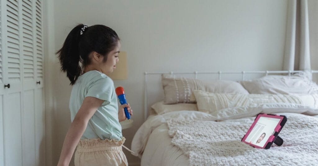 Young girl singing passionately with a toy microphone in a cozy bedroom.
