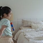 Young girl singing passionately with a toy microphone in a cozy bedroom.