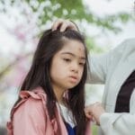 Mother gently helps her daughter adjust her hair during outdoor quality time.