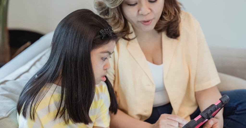 A mother and daughter engaged with a tablet, sitting on a couch, highlighting family bonding and technology.