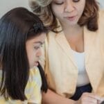 A mother and daughter engaged with a tablet, sitting on a couch, highlighting family bonding and technology.