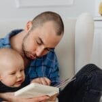 A father and his baby enjoy a bonding moment while reading together indoors.