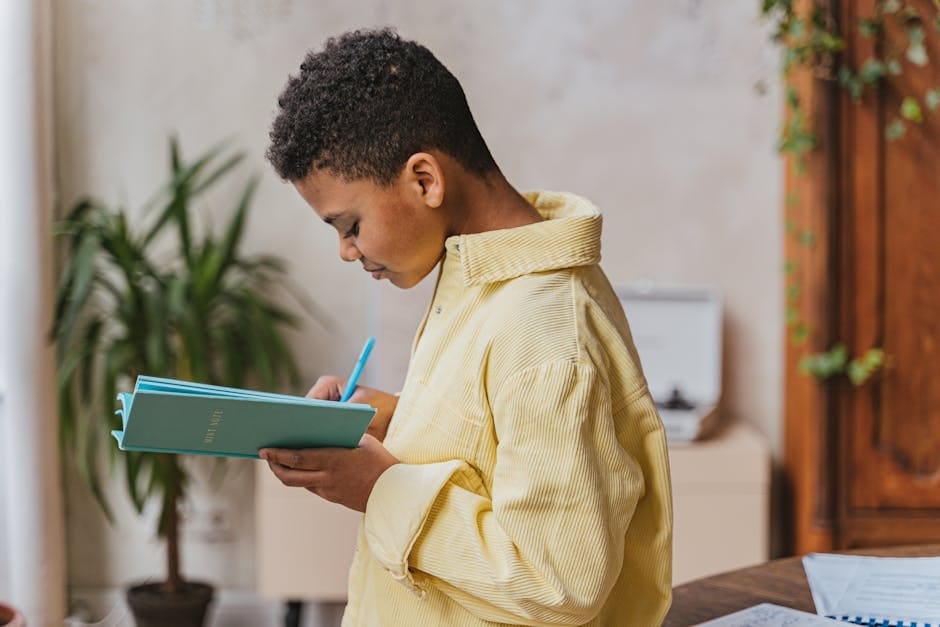 A young boy writing in a notebook while standing indoors, focused and engaged.