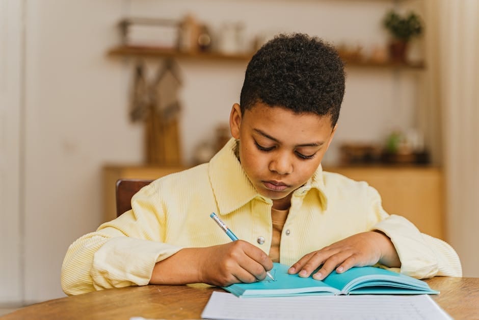 A young boy with curly hair focused on writing in a notebook at home.