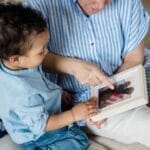 Grandmother and toddler bonding while looking at family photos on the sofa.