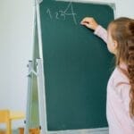 A young girl writing numbers on a classroom chalkboard, focusing on learning and education.