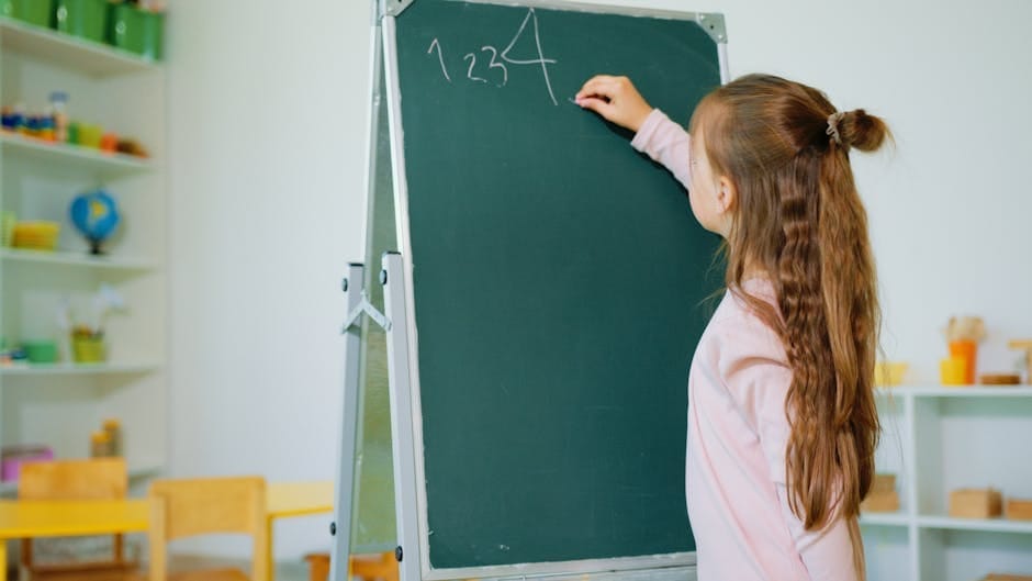 A young girl writing numbers on a classroom chalkboard, focusing on learning and education.