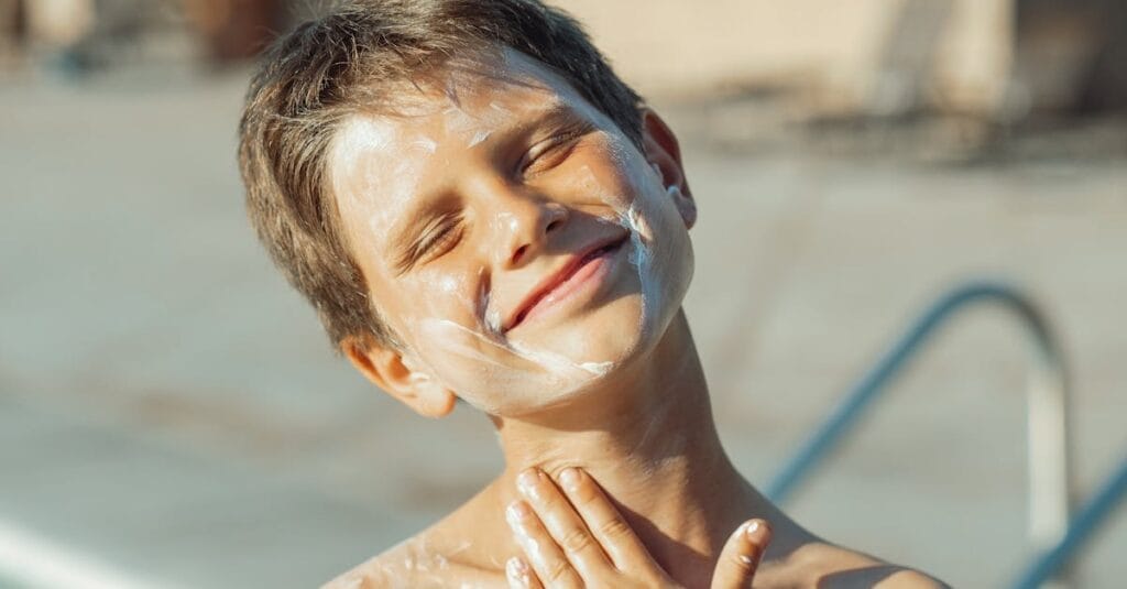 Smiling boy applying sunscreen, enjoying sunny day by the pool.