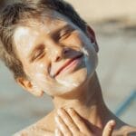 Smiling boy applying sunscreen, enjoying sunny day by the pool.