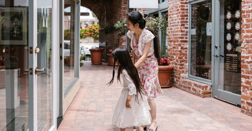 A mother and daughter window shopping in a charming urban brick-lined walkway.