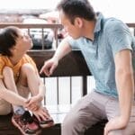 A heartfelt interaction between father and son sitting on a wooden bench outdoors, promoting bonds and autism awareness.