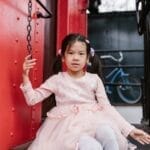 A young girl in a pink dress sits on a vintage train, evoking a sense of adventure and nostalgia.