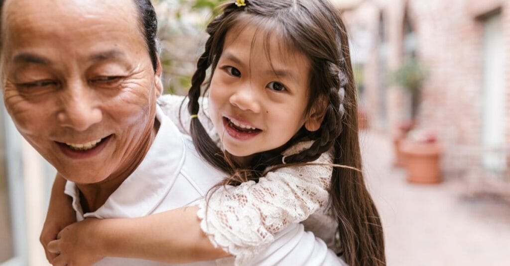 Happy girl enjoying a fun piggyback ride with her grandparent in an outdoor setting.