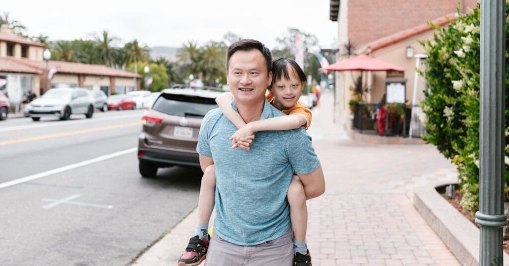 A joyful Asian father giving his child a piggyback ride on a city street.