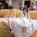 Children enjoying a sunny day sitting on hay bales, creating a relaxed and joyful atmosphere.