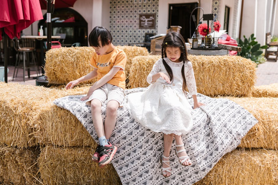 Children enjoying a sunny day sitting on hay bales, creating a relaxed and joyful atmosphere.