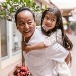 A cheerful moment between an older man and a child enjoying a piggyback ride in a cozy arcade setting.