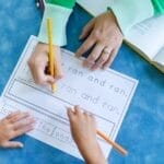 Child tracing letters with teacher guidance in a school setting.